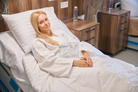 Photo for Portrait of pretty female patient lying on medical bed and waiting for medication treatment while looking at camera - Royalty Free Image