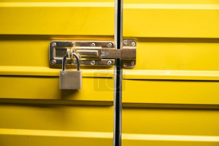 Closeup of square closed padlock hanging on yellow metal cargo container door latch