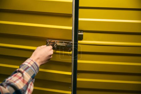 Primer plano de la persona cerradura a mano pestillo de metal en la puerta del contenedor de carga amarillo