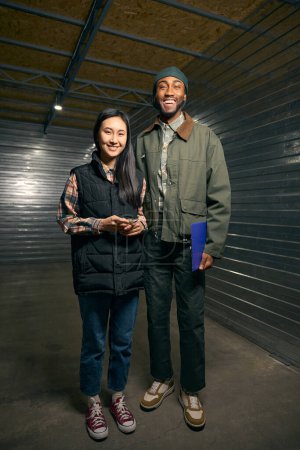 Full-size portrait of joyous warehouse manager with clipboard and happy tenant with door padlock in hand standing in shipping container