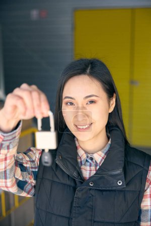 Retrato de una joven asiática sonriente sosteniendo un candado con llave en la mano