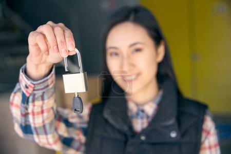 Retrato de una joven empleada de almacén sonriente sosteniendo la cerradura con llave en su mano
