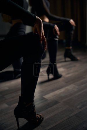 Foto recortada de trío de baile en traje negro en tacones altos realizando rutina de baile en suelo de parquet