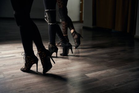 Cropped photo of dancing trio in black leggings and high heels standing in bevel pose on parquet floor