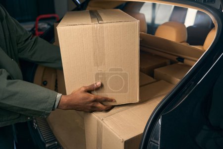 Young African man disassembles boxes with things from a machine. Cropped photo