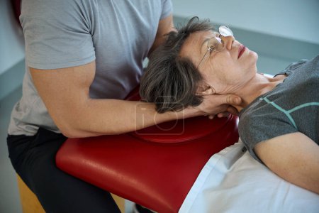 Rehabilitologe arbeitet mit den Halswirbeln einer älteren Frau, der Mann hat starke Arme