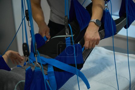 Employee of the fitness clinic placed the patient on a harness, using modern equipment