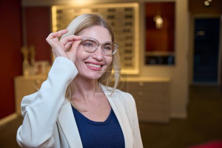 Blonde Frau probiert Brille in stylischem Rahmen an, es gibt eine große Auswahl in der Optik