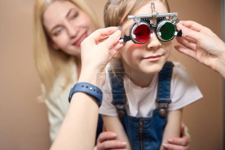 Augenarzt untersucht Kinderaugen mit einem speziellen Gerät, das Mädchen liegt in den Armen der Mutter