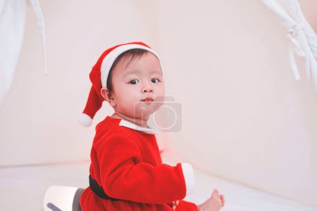 Photo for Asian baby girl in a Santa costume. Beautiful little baby celebrates Christmas. Christmas baby. - Royalty Free Image