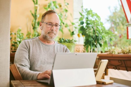 Photo for Portrait of middle age man working from home, using portable computer and mobile phone - Royalty Free Image