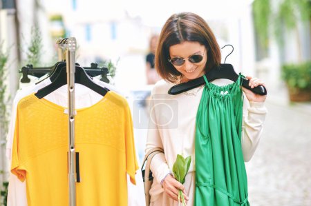 Happy mature woman buying clothes hanging for sale outside store
