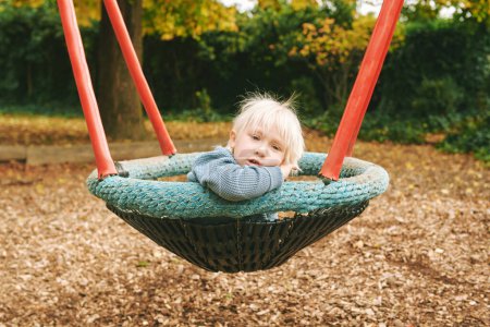 Outdoor portrait of adorable little sad boy relaxing on swing on playground