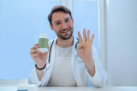 Foto de Retrato en la cintura de un médico general alegre con la botella de vitamina plástica en la mano durante la consulta - Imagen libre de derechos