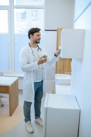 Téléchargez les photos : Portrait complet d'un médecin en blouse de laboratoire mettant des compléments alimentaires sur l'étagère murale - en image libre de droit