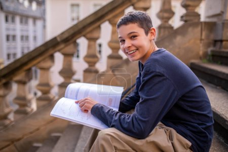 Cheerful teenager sitting on the stairs pointing his index finger at the task line in an open geometry textbook