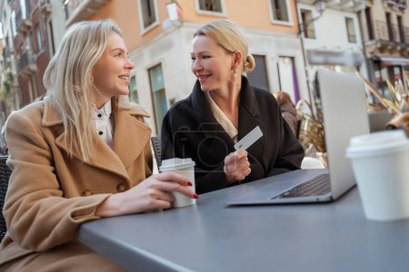 Photo for Meeting outside. Two blonde well-dressed women sitting in a street cafe - Royalty Free Image