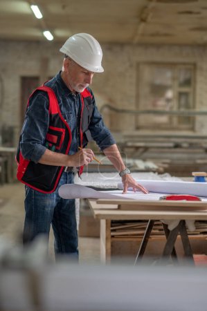 Photo for Work on project. Man in protective helmet working in a workshop with drawings - Royalty Free Image