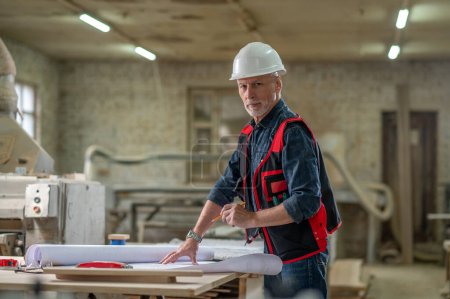 Photo for Work on project. Man in protective helmet working in a workshop with drawings - Royalty Free Image