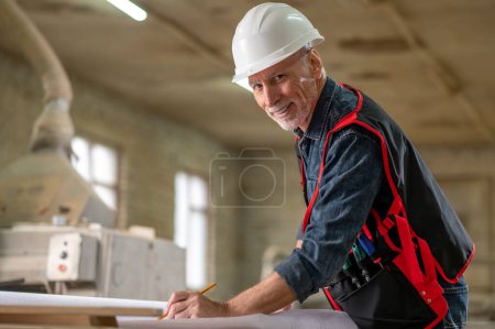 Photo for Work time. Mature man in protective helmet working in a workshop and looking contented - Royalty Free Image