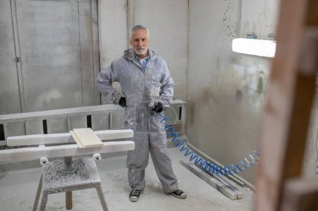 Téléchargez les photos : Peindre du bois. Homme en vêtements de protection travaillant dans un atelier de carpettes - en image libre de droit