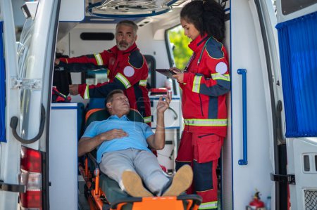 Téléchargez les photos : Médecine paramédicale saisissant les informations du patient dans la tablette en présence de son collègue - en image libre de droit