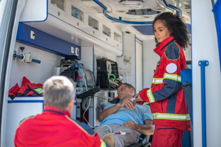 Foto de Médico de ambulancia serio mirando a su colega mientras mide el nivel de oxígeno en la sangre de un hombre inconsciente - Imagen libre de derechos