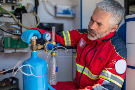 Téléchargez les photos : Médecin paramédical concentré sérieux dans les gants en nitrile tournant la vanne de bouteille d'oxygène dans le véhicule EMS - en image libre de droit