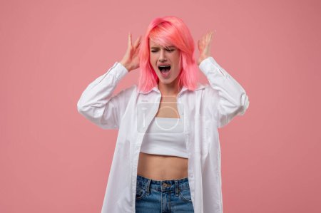 Téléchargez les photos : Jeune femme nerveuse en colère avec une langue perçant debout contre le mur rose et criant - en image libre de droit