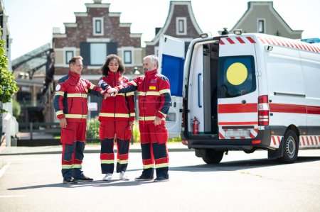 Photo for Smiling female paramedic and her colleagues standing outdoors and stacking their hands with their palms face-down - Royalty Free Image