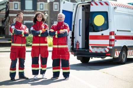 Glückliche Notärztin und ihre gut gelaunten Kollegen posieren neben dem Rettungswagen für die Kamera