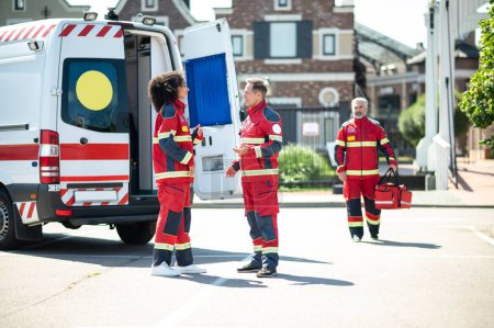 Téléchargez les photos : Médecins ambulanciers ayant une conversation à l'extérieur et attendant que leur collègue marche dans leur direction - en image libre de droit
