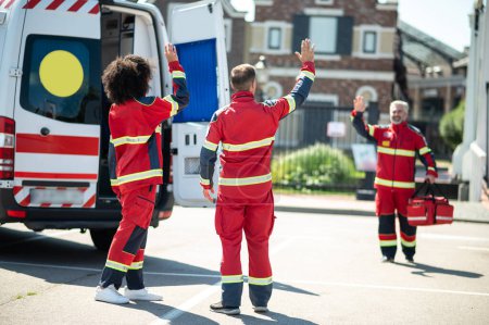 Photo for Gray-haired bearded paramedic with the EMS bag standing on the street and waving at his colleagues - Royalty Free Image