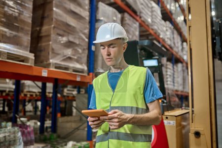 Foto de Retrato en la cintura de un trabajador serio de un almacén enfocado mirando la tableta en sus manos - Imagen libre de derechos
