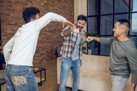 Photo for Company of cheerful guys playing the rock paper scissors while standing in a circle in the room - Royalty Free Image