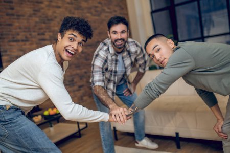 Photo for Smiling joyful Arab guy playing rock paper scissors with his pals in the living room - Royalty Free Image