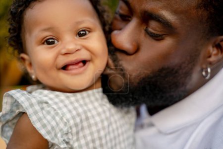 Photo for Bearded young African American man giving a kiss to his adorable smiling happy little child - Royalty Free Image