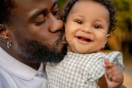 Affectueux jeune afro-américain mâle parent embrasser son sourire heureux bébé mignon sur la joue