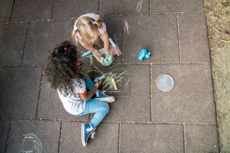 Photo for Top view of interracial friends sitting on the ground and choosing colored chalks for drawing - Royalty Free Image