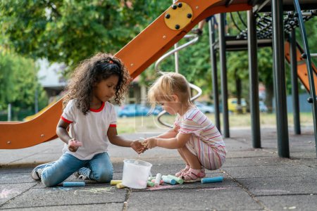 Photo for Little blonde child assisting her cute serious curly-haired friend in choosing varied colored chalks for drawing - Royalty Free Image