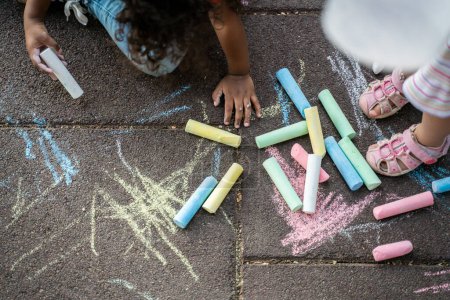 Photo for Cropped photo of a curly-haired child drawing with colored chalks on the ground in presence of a friend - Royalty Free Image
