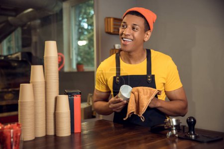 Téléchargez les photos : Portrait taille haute d'un travailleur de café joyeux essuyant une tasse en céramique avec une serviette en microfibre - en image libre de droit