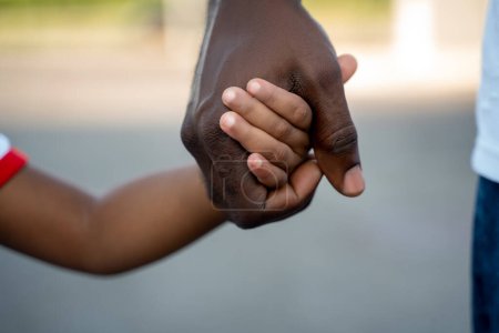 Photo recadrée d'un homme afro-américain adulte tenant un enfant par la main pendant la promenade