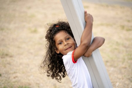 Photo for Cute curly-haired child holding on to the metal post and looking in front of her - Royalty Free Image