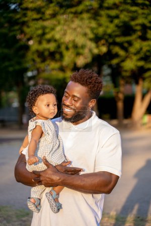 Photo for Smiling contented bearded young male parent looking at his adorable little child in his arms - Royalty Free Image