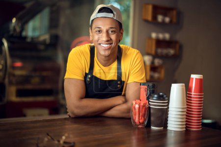 Téléchargez les photos : Portrait taille haute d'un travailleur souriant heureux café appuyé sur une table en bois et regardant devant lui - en image libre de droit