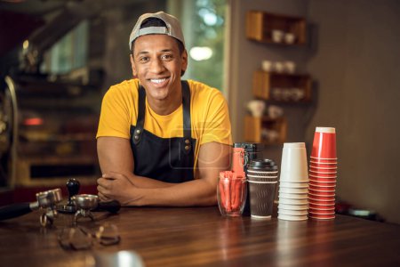 Foto de Retrato en la cintura de un trabajador de café feliz apoyado en la mesa y mirando delante de él - Imagen libre de derechos