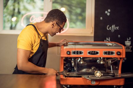 Foto de Retrato de cintura hacia arriba de un técnico enfocado con una llave en la mano mirando la máquina de café - Imagen libre de derechos
