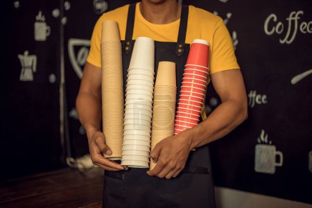Foto de Foto recortada de un camarero sosteniendo una pila de tazas de café desechables invertidas en sus manos - Imagen libre de derechos
