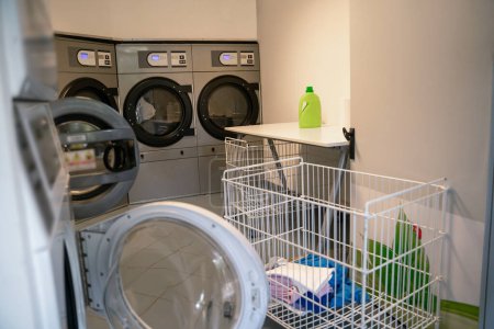 Foto de Interior moderno de una lavandería de autoservicio pública con varias lavadoras y carros de ropa metálicos - Imagen libre de derechos